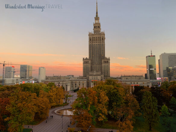 Gothic skyscraper surrounded by modern glass skyscrapers, a park with autumn foliage at dusk 