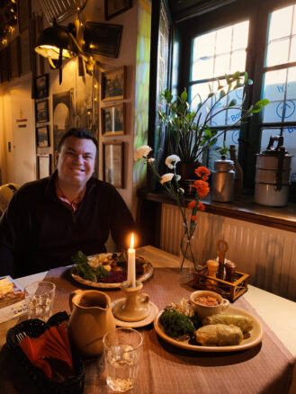 Alex sits at a candle lit table with two plates of food, one with stew and the other stuff cabbage