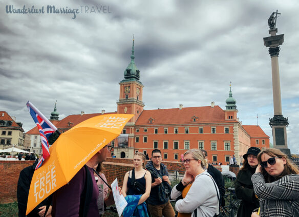 Guy holding a yellow umbrella advertising free walking tours as a group of tourists surround him with a historic building the background and stormy skies