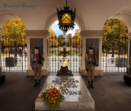 Two guards stand at attention next to a flame of remembrance, the trees in the background have golden leaves of autumn