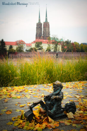 A bronze statue of gnome on a digger with autumn leaves in his digger with cathedral towers in the background