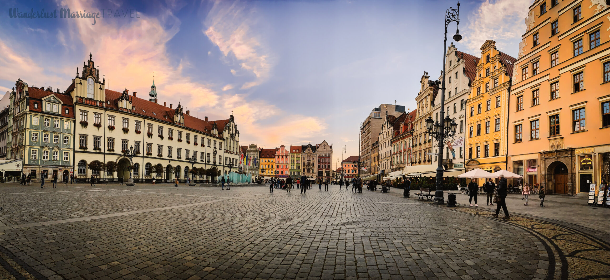 open cobble stoned square with colorful buildings on the perimeter and people walking through the square 