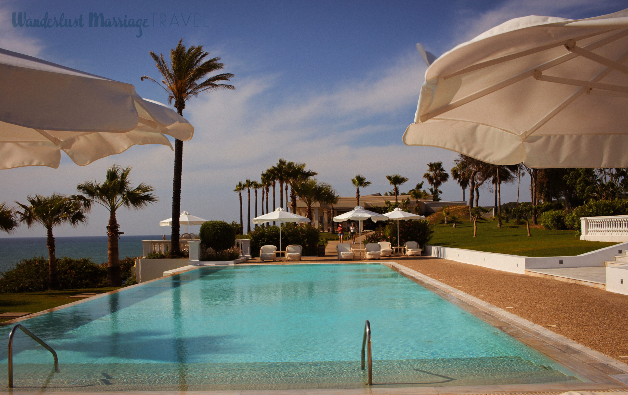 Crystal blue swimming pool, with umbrellas and sunbeds, with a view of the ocean and palm trees