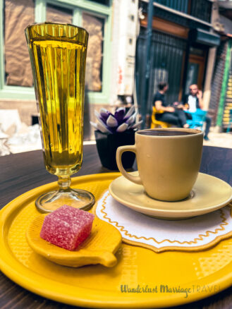 yellow coffee cup on a yellow plate, with a yellow water glass and a yellow leaf with a red sweet at a coffee shop