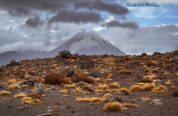 Snow capped volcano with intense cloud and a barren earth with golden brush