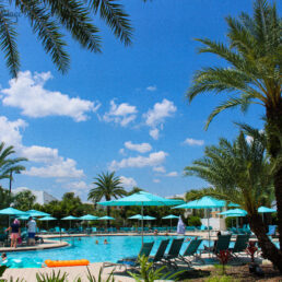 The large pool at Margaritaville Resort Orlando has many palm trees and umbrellas alongside it.