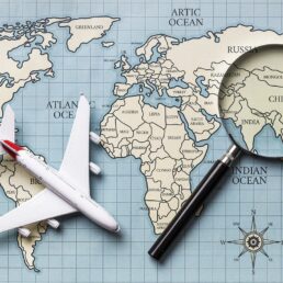 An Airplane and magnifying glass atop a world map.