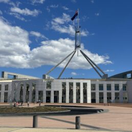 The exterior and entrance to the Parliament of Australia in Canberra on a day with a blue sky and puffy shite clouds.