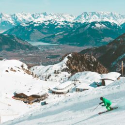 A skier going down a ski slope with snow capped mountains in the distance.