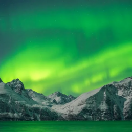 Green colors dominate the Northern Lights over snow capped mountains near Tromso, Norway.