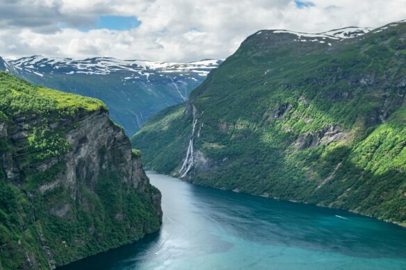A river valley amidst the beautiful Norwegian Fjords with a mostly cloudy sky above.