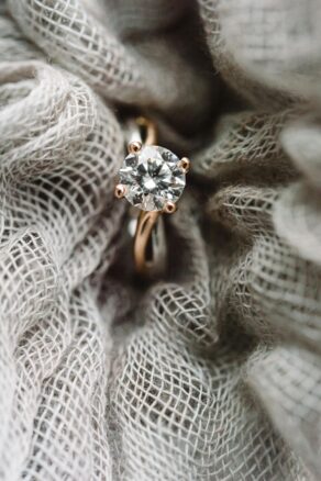 A vintage engagement ring with a round diamond and gold band atop a grey cloth.