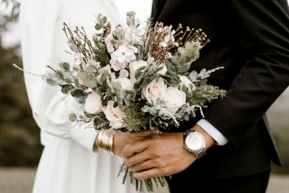 A couple holds a wedding bouquet with white and pink flowers together.
