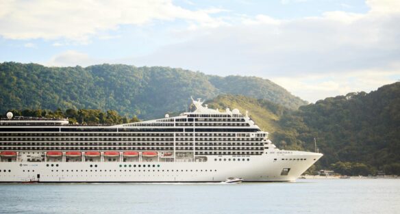 A cruise ship sails past a small forested mountain.