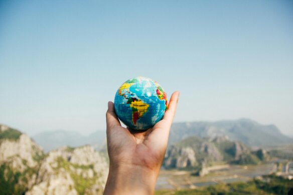 Someone holding a mini globe in their hand, with mountains in the background.