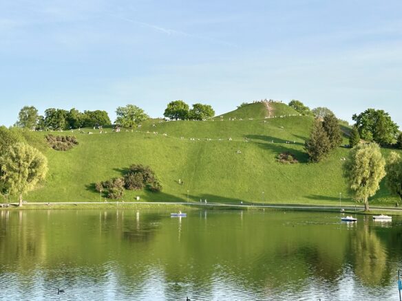 A large hill dotted with trees amidst ample green space in Olympiapark in Munich, Germany