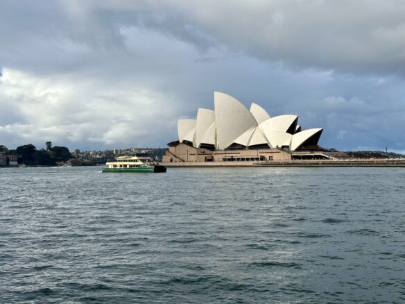A ferry passes the Sydney Opera House with a cloudy Sky over picturesque Circular Quay.