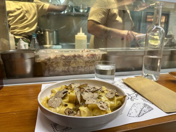 A plate of carbonara pasta with a view of the kitchen preparing meals at San Maurizio 1619 Truffle Bistrot inside Marché De La Condamine.