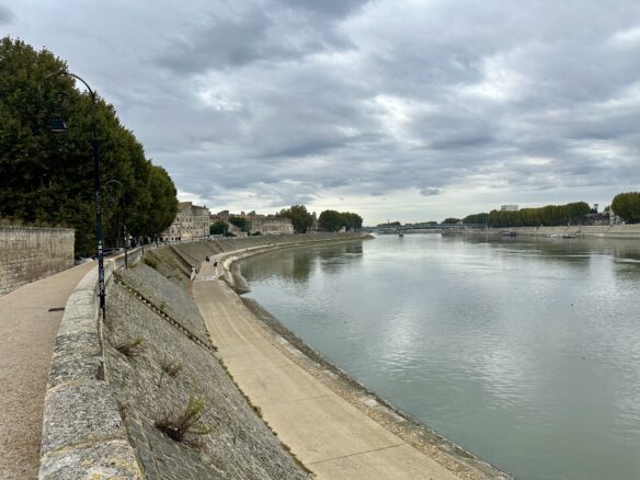 The Rhone River winds through Arles, France with a cloudy sky above.