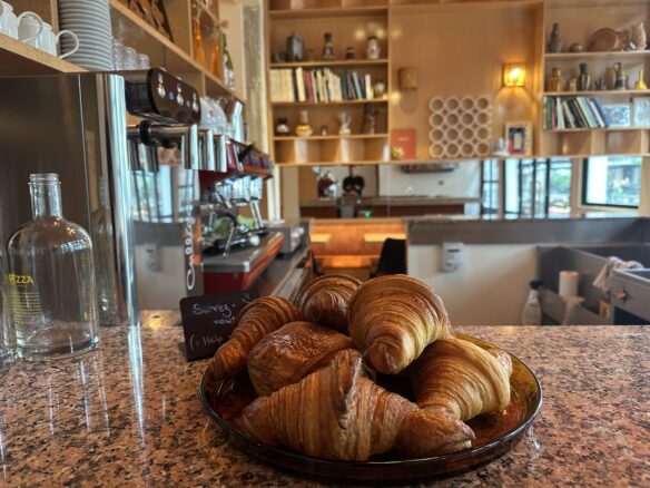 A pile of croissants in the lounge of Hotel Present with a coffee machine and library in the background.