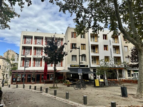 The center of Arles, France including Hotel Present with a partly cloudy blue sky overhead.