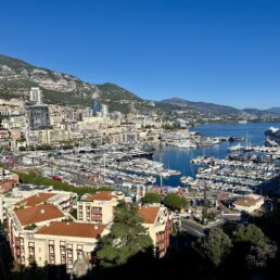 Sweeping view overlooking Monte Carlo, the marina and a cruise ship from Monaco City with a blue sky above.