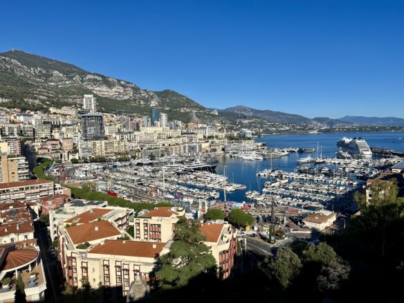 Sweeping view overlooking Monte Carlo, the marina and a cruise ship from Monaco City with a blue sky above.