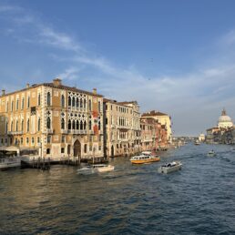 Boats sail down the Grand Canal in Venice, Italy with a blue partly cloudy sky.