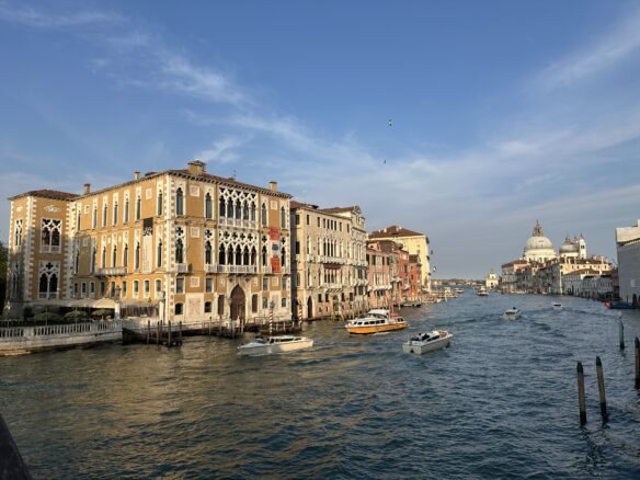 Boats sail down the Grand Canal in Venice, Italy with a blue partly cloudy sky. 