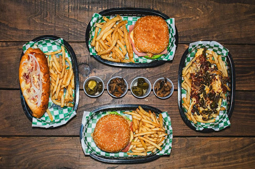 Four different meals with fries, including two burgers, a focaccia and nachos with four condiments in the middle. 