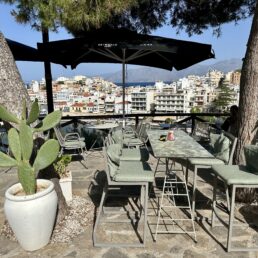 A cafe terrace overlooking Agios Nikolaos, Crete, the Mediterranean Sea and mountains.