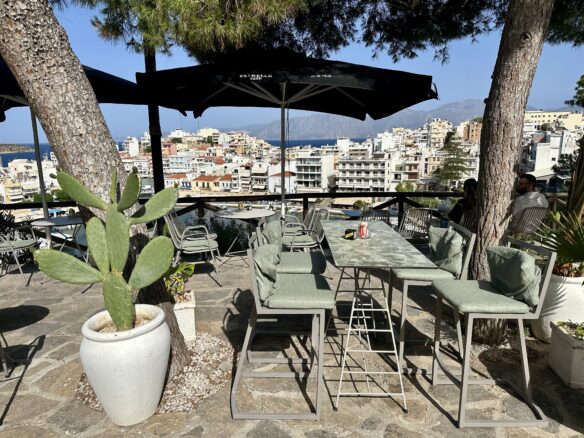 A cafe terrace overlooking Agios Nikolaos, Crete, the Mediterranean Sea and mountains.
