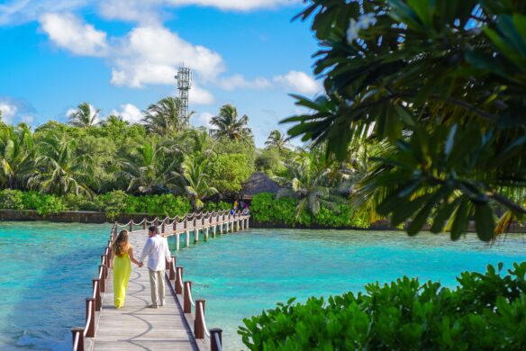 A couple holding hands while walking on a wooden bridge over turquoise water.