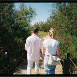 A couple walking along a wooden bridge in a forested park.