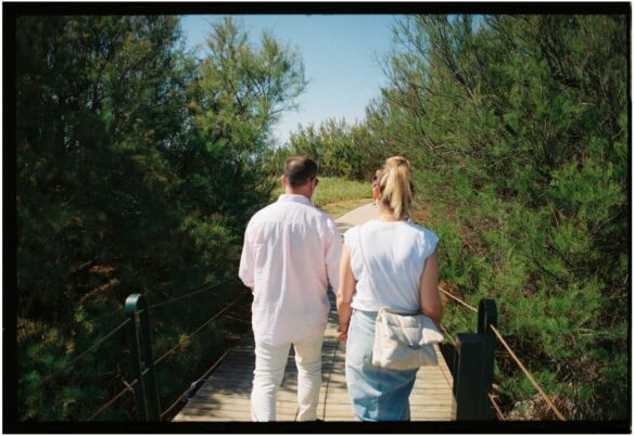 A couple walking along a wooden bridge in a forested park.