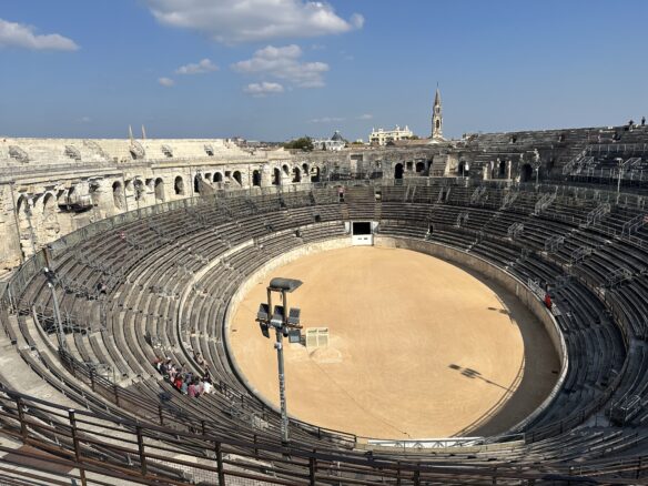 The interior of the Arena of Nimes from the top bleachers, with part of Nimes in view across the horizon.